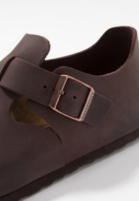 Brown leather clog with an adjustable strap and bronze buckle. Features a contoured cork footbed and a textured rubber outsole.