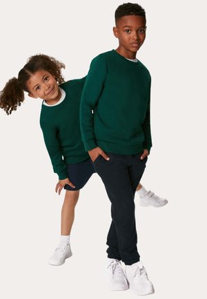 To børn har matchende mørkegrønne sweatshirts lavet af blødt stof, med rund halsudskæring, parret med marineblå bukser og hvide sneakers.