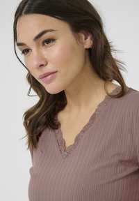 Top de mujer en color malva con canalé, escote en V y borde de encaje. La tela tiene una textura suave y un diseño ajustado que realza el escote y los hombros.