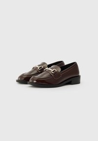 Mocassins en cuir verni marron avec un petit talon carré, dotés d'une boucle décorative sur le devant et d'une finition lisse et brillante.