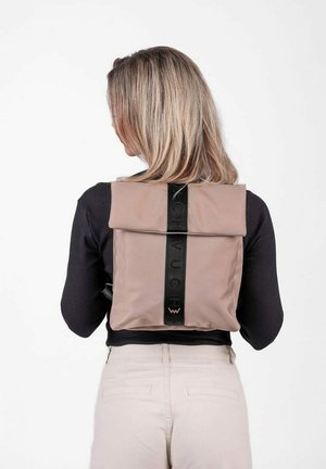 Kompaktní batoh z jemného béžového materiálu, s rolovacím uzávěrem a kontrastním černým popruhem s nápisem. Minimalistický design, hladká textura.