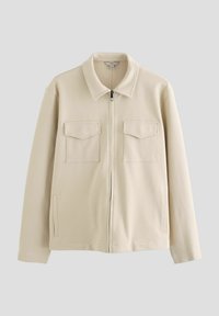 Chaqueta beis con cremallera, cuello tipo solapa, dos bolsillos en el pecho y bolsillos laterales. Fabricada en una tela suave y texturizada.