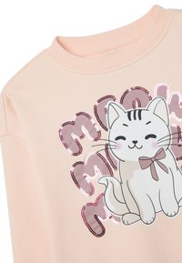 Sweatshirt rose avec un dessin de chat en cartoon portant un nœud, orné de sequins formant le mot "meow". Texture douce, col rond et coupe décontractée.