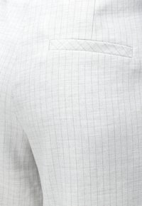 Κοντινή λήψη ανοιχτόχρωμου γκρι υφάσματος με ρίγες και μικρή τσέπη με welt, που αναδεικνύει την υφή και τις λεπτομέρειες της ραφής.