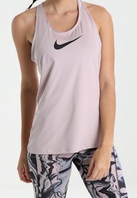 Top sportivo di colore rosa chiaro con il logo Nike nero. Presenta un design a schiena scoperta e un tessuto morbido e traspirante. Abbinato a leggings con motivo.