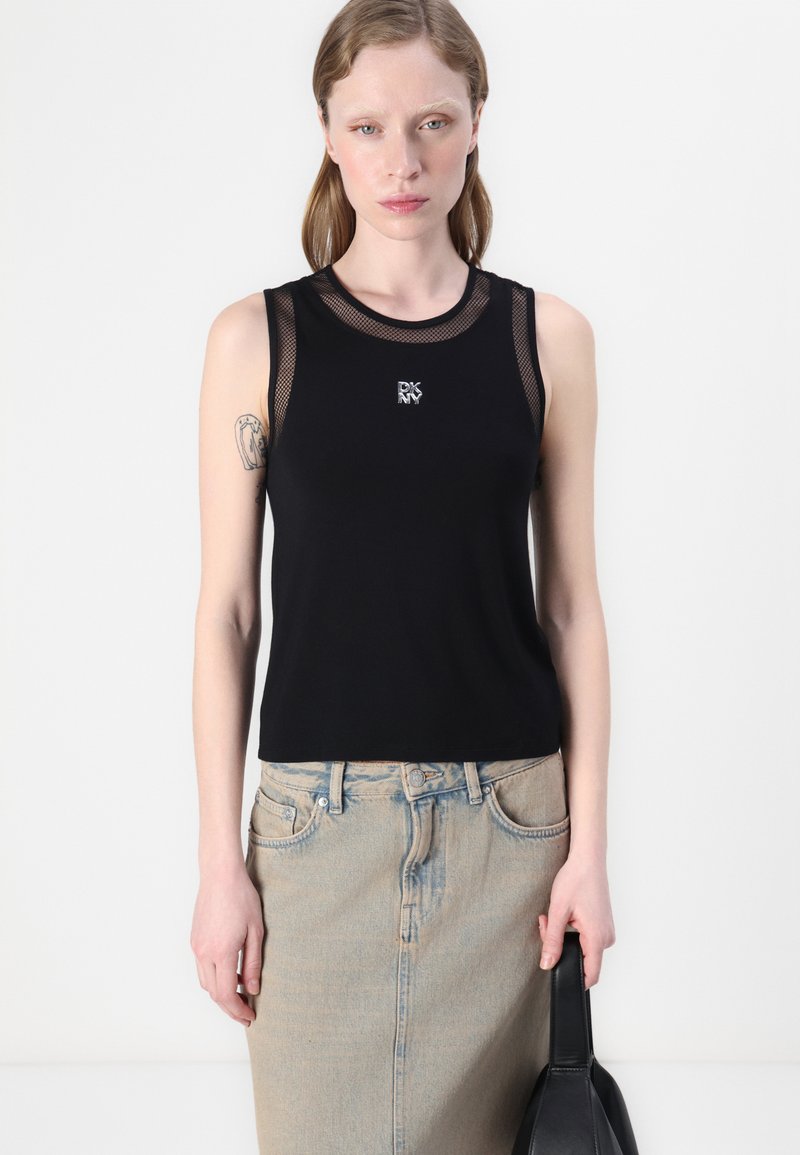 Top negro sin mangas con detalles de malla y un logo en el pecho, combinado con una falda de mezclilla azul clara. Tela suave con un diseño ajustado.