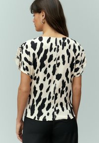Haut à manches courtes en imprimé animal noir et blanc, en tissu texturé avec des manches volantes, présentant un dos droit et un ourlet arrondi.