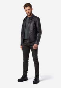 Svart läderjacka med dragkedja fram, platt krage och dragkedjefickor. Bärs över en mörkgrå skjorta, i kombination med svarta jeans och stövlar.