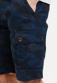 Blå camouflage cargo shorts med en tekstureret stof, der har vandrette striber, to sidelommer med knaplukninger og en afslappet pasform.
