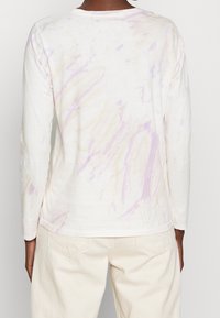 Pitkähihaisessa, kermaisenvärisessä paidassa on vaaleanvioletti ja keltainen necktie-dye-kuvio. Pehmeä, teksturoitu kangas ja pyöreä pääntie.