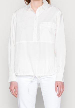 Witte, langharige blouse met knoopsluiting, borstzak en elastische boord onderaan. Gemaakt van een gladde stof en heeft een ontspannen pasvorm.
