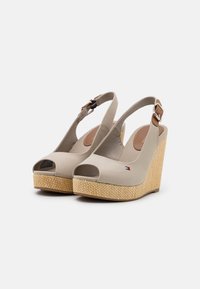 Sandali beige con zeppa, apertura sulla punta, cinturino alla caviglia e una piattaforma in stile juta intrecciata. Presentano un piccolo logo sul lato.