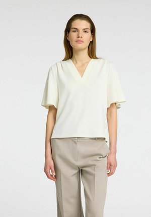 Witte V-hals blouse met korte vlinder mouwen, gemaakt van een gladde stof. Draagt met lichtbeige op maat gemaakte broeken met een ontspannen pasvorm.