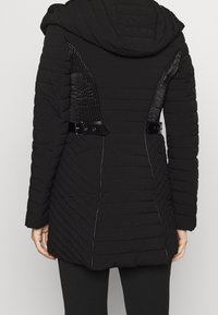 Czarna kurtka puchowa z kapturem, o pikowanej fakturze, z prążkowanymi panelami bocznymi oraz czarnymi akcentami z metalowymi elementami, z regulowanymi paskami po bokach.