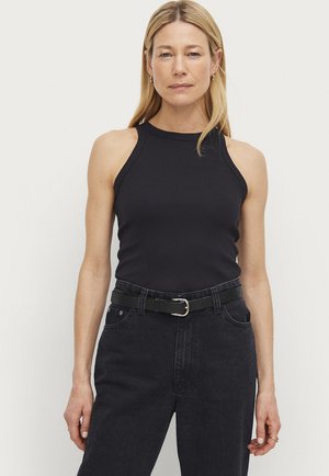 Schwarzes, geripptes Tanktop mit hohem Kragen, kombiniert mit dunklen Jeans und einem schwarzen Gürtel mit einer silbernen Schnalle. Glatte Textur, taillierte Passform.