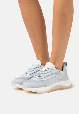 Light gray sneakers with a textured upper, rubber sole, and white accents. Features laces and branding on the side.