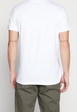 T-shirt en coton blanc à manches courtes et col rond, présenté de dos. Tatouages remarquables de fil barbelé sur les bras.