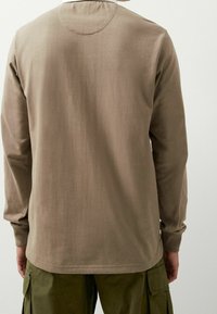 Camicia a maniche lunghe taupe con scollatura rotonda, in morbido cotone e design semplice, indossata con pantaloni cargo verdi oliva.