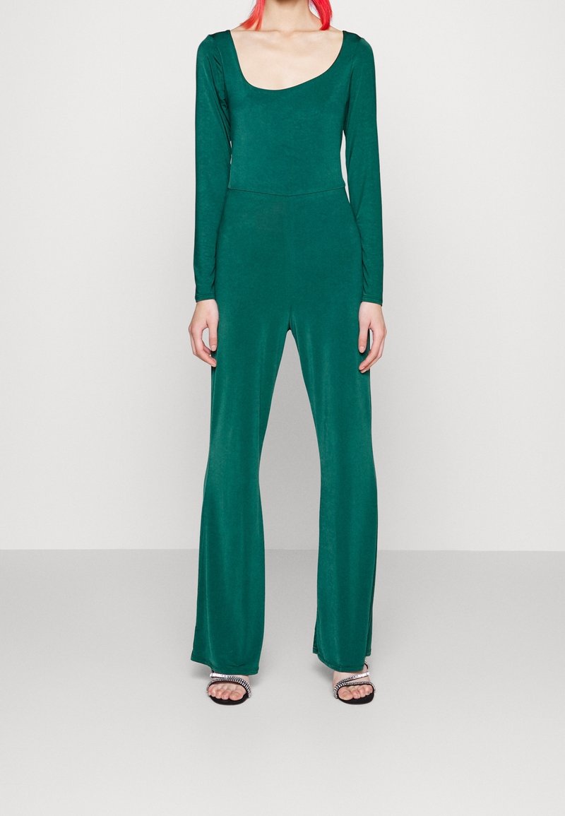 Combinaison verte à manches longues avec un col arrondi, un corsage ajusté, des jambes larges et fluides, fabriquée dans un tissu lisse et extensible.