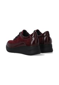 Par af mørkerøde ruskinds- og laklæder-platform-sneakers med sorte tykke såler, vist fra bagsiden på en hvid baggrund.
