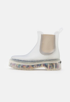 Bottine translucide à la cheville avec panneau latéral élastique beige et semelle remplie de morceaux colorés de plastique recyclé, présentée sur fond blanc.