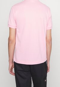Polo rosa de manga corta con un corte relajado, textura suave y puños enrollados. Presenta dobladillo recto y un detalle de costura en la parte posterior del cuello.