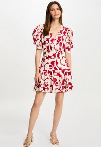 Korte mouwen jurk in het wit met gedurfde rode abstracte bloemenprint. Beschikt over een V-hals, gerimpelde pofmouwen en een uitlopende rok.