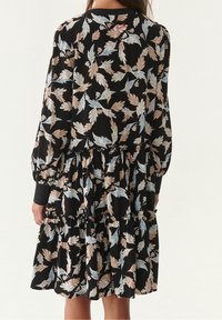 Vestido negro de manga larga, con un diseño de capas y un estampado floral en hojas de azul claro y beige. Textura de tela suave.