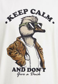 Grafisk T-shirt med en tegneserieand i grønne solbriller og en brun jakke, med teksten "BLIV ROFYLDT OG GIV IKKE EN AND."