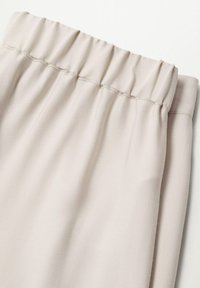 Pantalons en tissu beige avec une taille élastique et des coutures visibles sur un fond blanc.