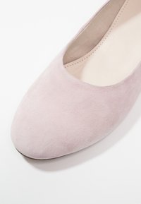 Chaussure plate en daim rose clair avec un bout arrondi et un design à coupe basse, dotée d'une doublure intérieure lisse et de détails de couture minimalistes.