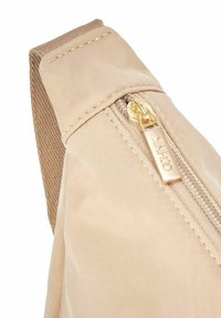 Beżowa torba na ramię z tkaniny z złotym zamkiem błyskawicznym i teksturowanym paskiem. Projekt obejmuje staranne przeszycie i gładkie wykończenie powierzchni.