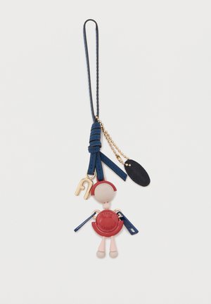Μπρελόκ με μικρή φιγούρα κούκλας που φοράει κόκκινο φόρεμα, μπλε δερμάτινο λουρί, χρυσό κούμπωμα και χρυσή αλυσίδα με μαύρη ετικέτα.
