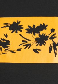 Tecido preto com uma faixa horizontal laranja com impressões florais pretas. O design inclui várias formas de folhas e contornos de flores.