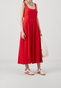 Robe sans manches en lin rouge avec une silhouette fluide, associée à des baskets blanches à rayures rouges et un sac à main couleur crème.