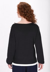 Black sweater with a wide neckline, long sleeves, and a white hem. Features gold accents on the shoulders. Smooth texture and casual design.