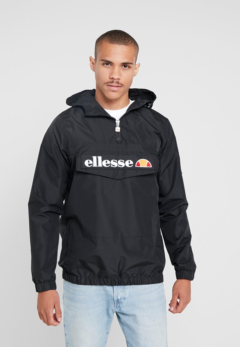 Svart vindjakke med hette, med en frontlomme for hånden og brodert "ellesse"-logo. Justerbare mansjetter og elastisk kant.