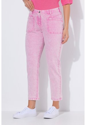 Kobieta w różowych jeansach z wysokim stanem i efektami wybielania, z frontowymi naszywanymi kieszeniami, ubrana w białe sneakersy i jasnoróżowy sweter.