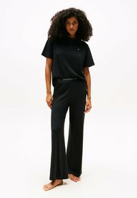 Zwart casual set bestaande uit een polo met korte mouwen en wijde broek. De tailleband heeft een logo-accent. Gemaakt van zachte stof.