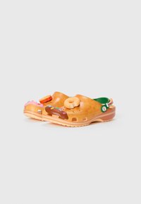 Orangene Kunststoffclogs mit 3D-Accessoires im Donut- und Dessertdesign, Belüftungsöffnungen und einem grünen Innenraum. Mit einem Fersenriemen.