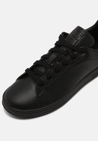 Sort lædersneaker med rund tå, detaljeret syning og snørebåndslukning. Har perforerede sider og en tekstureret sål for godt greb.