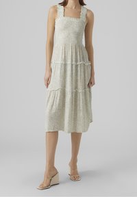 Kukallinen midi-mekko vaaleanvihreänä, joka tarjoaa korjattuja rintahihnoja, röyhelöisiä olkaimia ja kerroksellisen hameen. Yhdistettynä läpinäkyviin korkokenkiin.