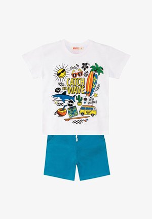 T-shirt bianca con una grafica colorata che presenta motivi legati al surf e testo; abbinata a pantaloni blu. Maniche corte e vestibilità casual.