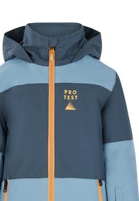 Mėlynas ir tamsiai žalias sukapotas džemperis su oranžiniu užtrauktuku, turintis "PRO TEST" logotipą ir trikampio dizaino detalę ant krūtinės.