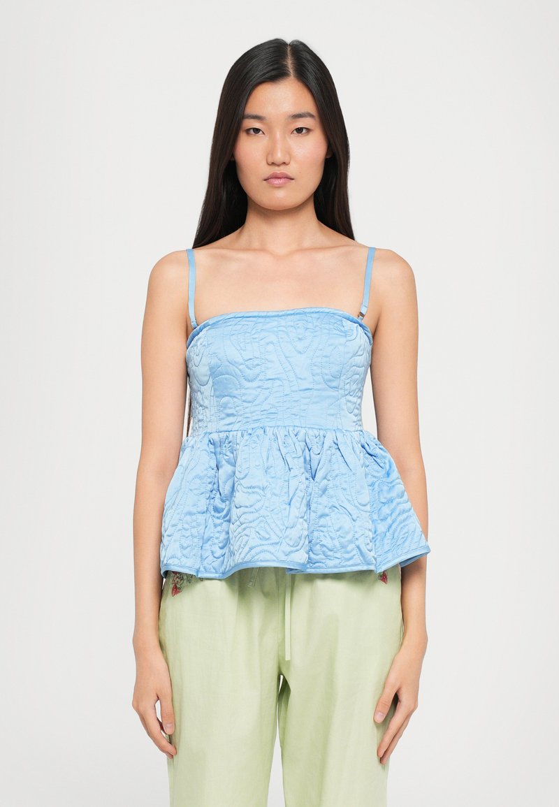 Top peplum de culoare albastru deschis, cu bretele subțiri, având un model texturat cu umplutură. Pur și simplu peste o pereche de pantaloni verzi, cu detalii florale subtile la tiv.