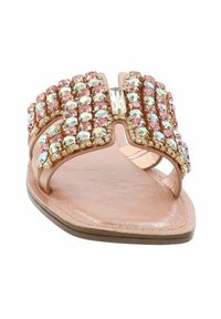 Infradito rosa pallido con suola piatta, dotata di una fascia arricchita di strass a forma di fiocco e un accento centrale di pietra trasparente.