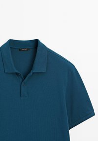 Modrá polokošile s krátkým rukávem, se dvěma knoflíky a žebrovaným límcem, položená na bílém pozadí.