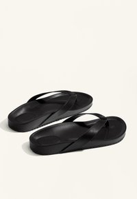 Sandale negre cu talpă plată și curele încrucișate. Fabricate din cauciuc cu o textură netedă și detalii minime de profil.