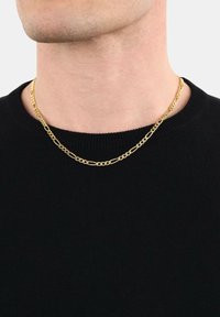 Primo piano del collo di una persona che indossa una collana di tipo Figaro in oro sopra un maglione nero a maniche corte.
