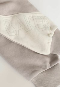 Gray and cream sweatshirt featuring a textured fabric, a diagonal design, and "BAKER" printed in a subtle, raised font on the cream panel.